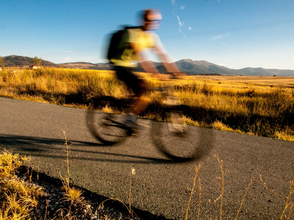 Ciclista en bicicleta de montaña por un camino en una ruta por la provincia de Segovia entre campos y la figura desenfocada.